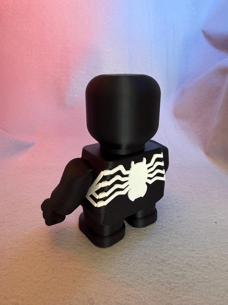 May include: Black and white 3D printed figurine of a superhero with a spider web design on the chest.