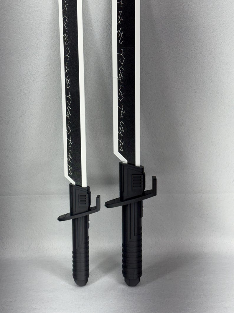 May include: Two black and white toy swords with a futuristic design. The blades are white with black edges and etched patterns. The handles are black with a ribbed texture and crossguard.