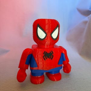 May include: A red and blue Spider-Man action figure with a black spider logo on the chest. The figure has a detailed face with white eyes and a red and black spider web pattern on the head.
