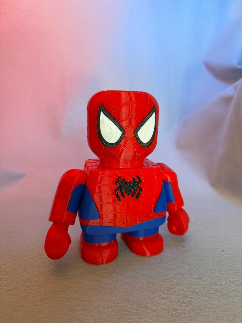 May include: A red and blue Spider-Man action figure with a black spider logo on the chest. The figure has a detailed face with white eyes and a red and black spider web pattern on the head.