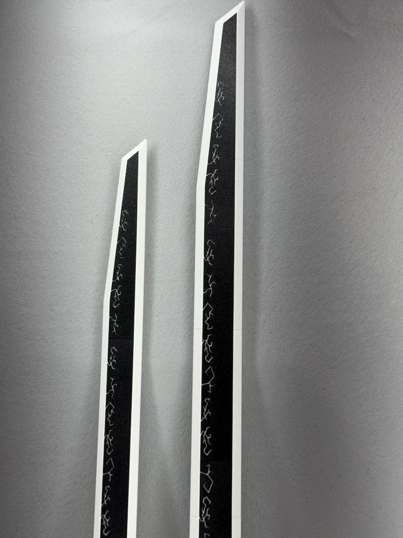 May include: Two tall, black and white abstract art pieces. The black sections feature white, stylized script. The pieces are set against a gray background. The shapes are long and angular, with a modern aesthetic.
