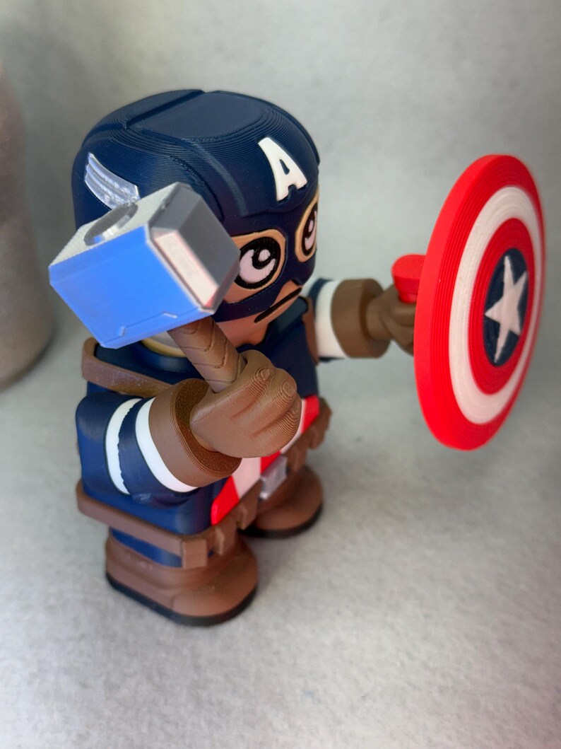 Op de afbeelding: Een 3D-geprinte Captain America-figuur, met een hamer en schild. De figuur is voornamelijk blauw, bruin en rood, met een witte ster op het schild. De helm heeft een witte "A".