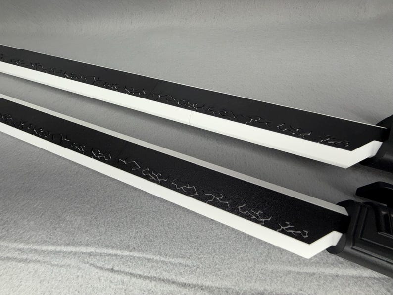 May include: Two black and white swords with decorative etchings along the black blade. The swords have a white edge and a black handle. The blades are angled towards the viewer.