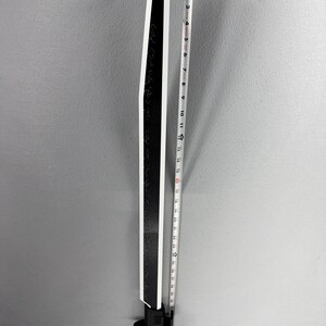 May include: A black and white sword with a straight blade. The blade has a white edge and is approximately 24 inches long. The handle is black and has a guard. The sword has etched markings on the blade.