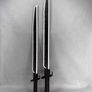 May include: Two black and white toy swords with a futuristic design. The blades are black with white edges and etched detailing. The handles are black with a textured grip. One sword is shorter than the other.