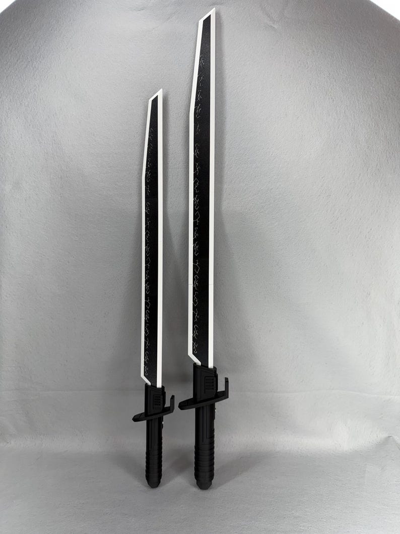 May include: Two black and white toy swords with a futuristic design. The blades are black with white edges and etched detailing. The handles are black with a textured grip. One sword is shorter than the other.
