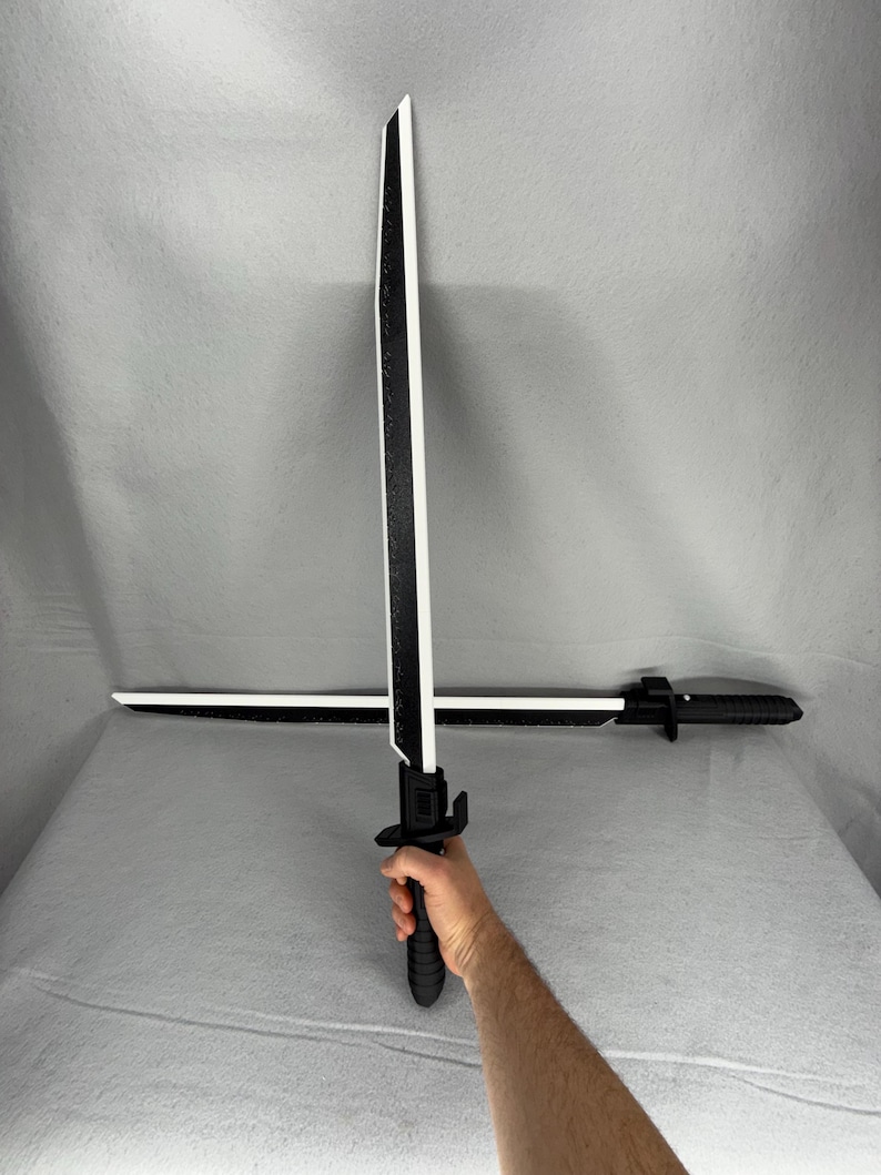 May include: Two black and white toy swords. The swords have a black handle and a white blade with a black stripe down the center. One sword is held by a person, and the other is lying horizontally.