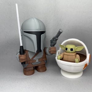 May include: A gray and brown Mandalorian action figure holding a blaster and a white lightsaber. The figure is standing next to a white and orange baby Yoda action figure sitting in a floating pod.