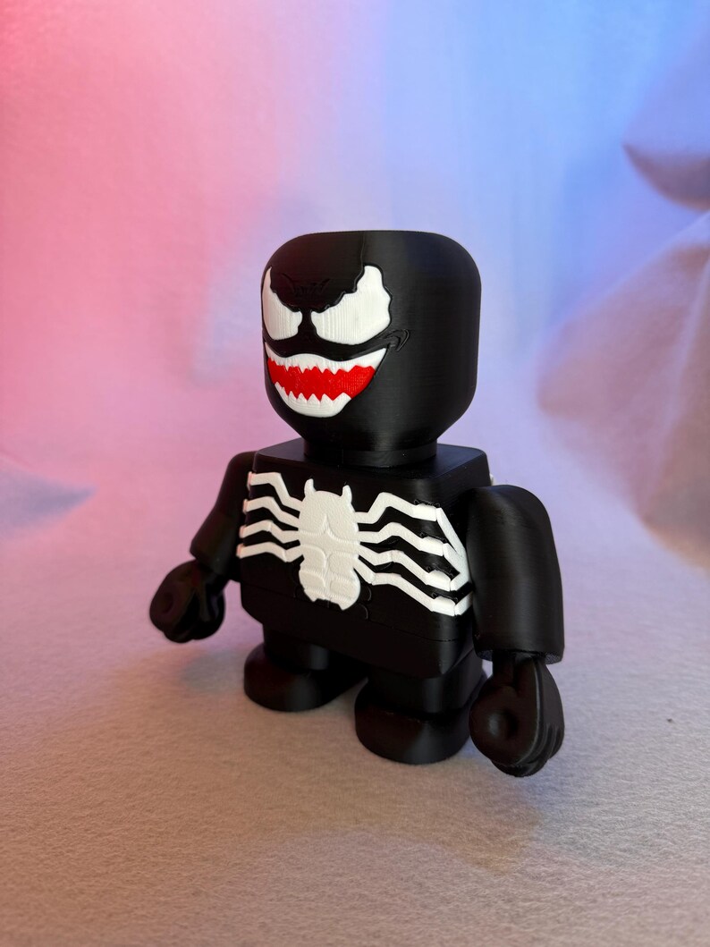 May include: A black and white 3D printed figurine of Venom, a Marvel Comics superhero. The figurine has a large head with a white spider symbol on the chest.