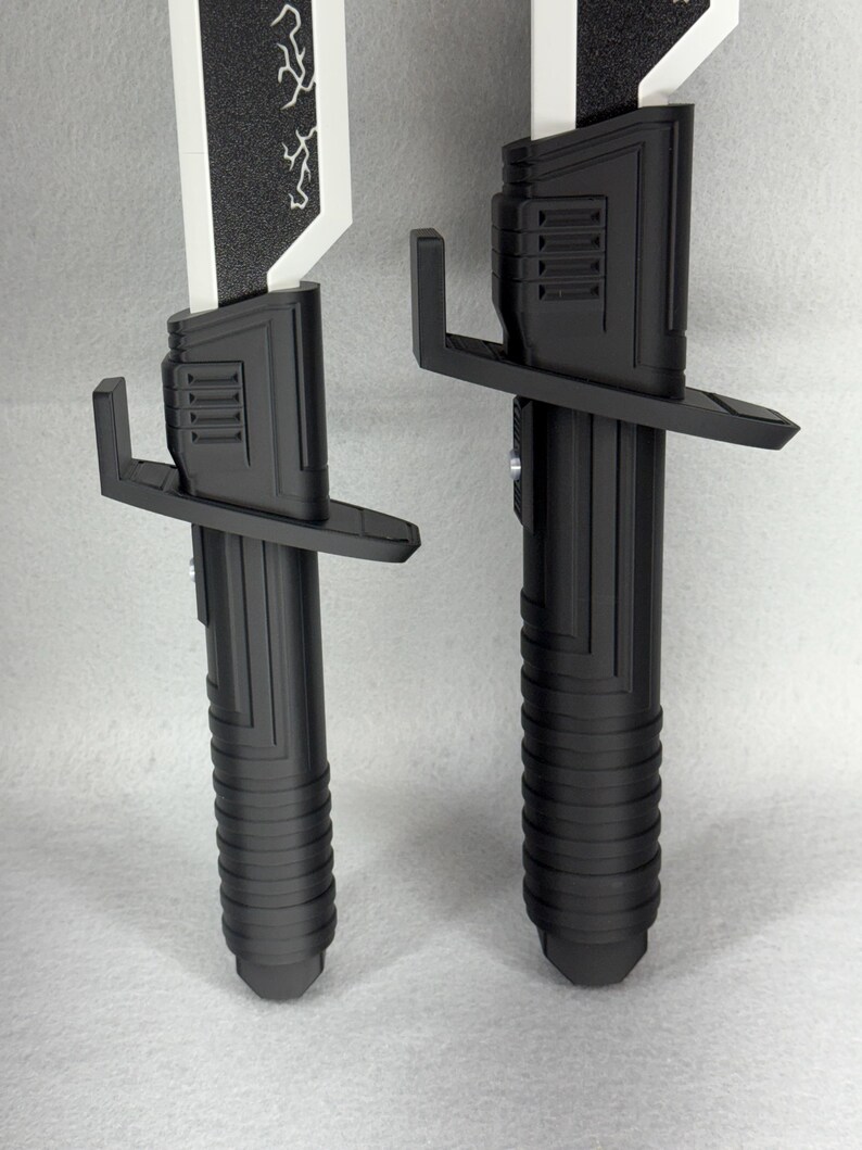 May include: Two black and white toy light sabers. The hilts are black with a ribbed design, and the blades are white with a black textured top. One blade has a lightning bolt design. The hilts have a crossguard.