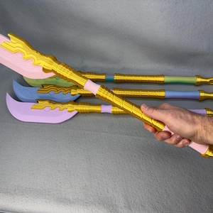 May include: A collection of decorative, fantasy-themed weapons in various pastel colors. The blades are pink, blue, and purple, with gold-colored accents. One is held by a hand, showcasing the gold handle and pink blade.