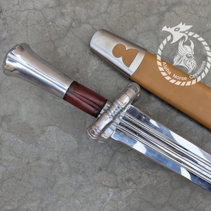 May include: A silver sword with a brown leather-wrapped handle and a tan leather sheath. The sword has a polished blade and a decorative hilt. The sheath has a silver cap with a cutout design. The sword is a Viking-style weapon.