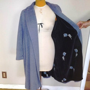 May include: A light blue wool coat with a black velvet lining featuring blue floral embroidery. The coat has a classic collar and long sleeves.