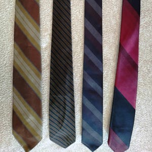 Può includere: Cinque cravatte in vari colori e fantasie. Le cravatte includono marrone con strisce gialle, nero con strisce marroni, blu navy con strisce grigie e un design diagonale rosso e nero. Le cravatte sono disposte verticalmente.