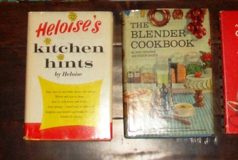 Puede incluir: Tres libros de cocina vintage con portadas coloridas. El primer libro se titula "Heloise's Kitchen Hints by Heloise" y presenta un dise&ntilde;o amarillo y rojo. El segundo libro se titula "The Blender Cookbook by Ann Seranne and Eileen Gaden" y presenta una ilustraci&oacute;n colorida de una licuadora y comida. El tercer libro es rojo y su t&iacute;tulo no es visible en la imagen.