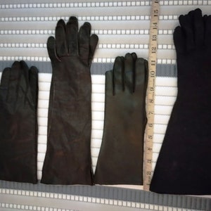 May include: Four pairs of black gloves of varying lengths are displayed. The gloves are made of leather and fabric. A ruler is placed next to the gloves to show their different lengths. The longest pair of gloves measures approximately 15 inches.