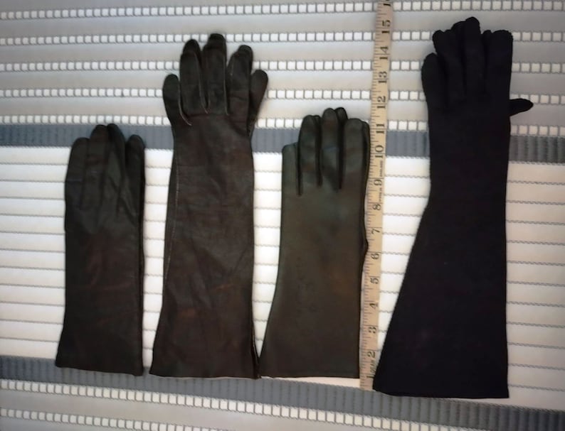 May include: Four pairs of black gloves of varying lengths are displayed. The gloves are made of leather and fabric. A ruler is placed next to the gloves to show their different lengths. The longest pair of gloves measures approximately 15 inches.