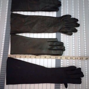 May include: Three pairs of black gloves are displayed. The top two pairs appear to be leather, with the middle pair showing some wear. The bottom pair is a darker, possibly fabric, material. A measuring tape is placed along the gloves.