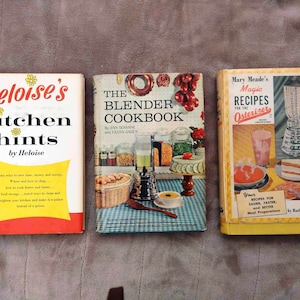 May include: Three vintage cookbooks with colourful covers. The first book is titled "Heloise's Kitchen Hints" with a yellow and red cover. The second book is titled "The Blender Cookbook" with a blue and white checked cover. The third book is titled "Mary Meade's Magic Recipes for the Osterizer" with a yellow and red cover.