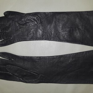 May include: A pair of black leather gloves, laid flat. The gloves have a long, sleek design, with a smooth texture. The gloves are likely for cold weather or formal occasions.