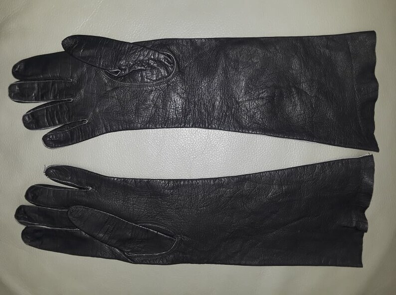 May include: A pair of black leather gloves, laid flat. The gloves have a long, sleek design, with a smooth texture. The gloves are likely for cold weather or formal occasions.