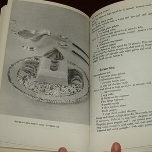 Puede incluir: Un libro de cocina vintage abierto en una p&aacute;gina con una receta para "Chicken Ring". La receta incluye ingredientes como gelatina sin sabor, jugo de cereza, caldo de pollo caliente, mostaza seca, piment&oacute;n y pollo cocido. La p&aacute;gina tambi&eacute;n presenta una foto en blanco y negro de un pastel de pollo y zanahoria.