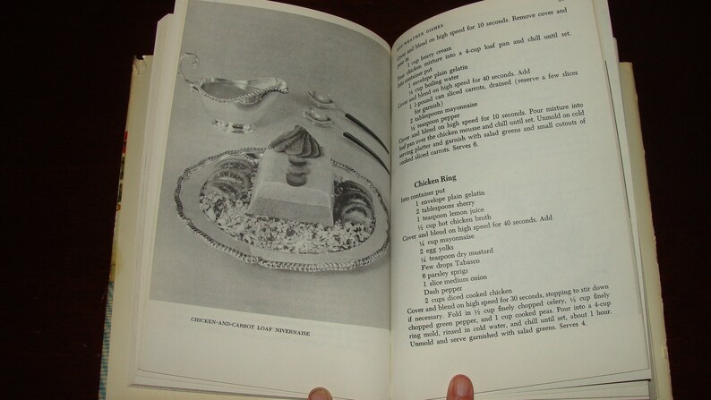 Puede incluir: Un libro de cocina vintage abierto en una p&aacute;gina con una receta para "Chicken Ring". La receta incluye ingredientes como gelatina sin sabor, jugo de cereza, caldo de pollo caliente, mostaza seca, piment&oacute;n y pollo cocido. La p&aacute;gina tambi&eacute;n presenta una foto en blanco y negro de un pastel de pollo y zanahoria.
