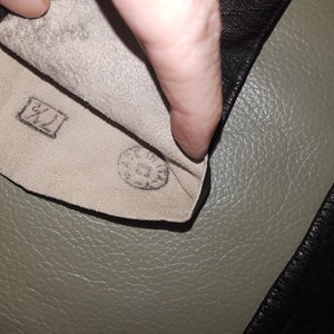 May include: Close-up of the inside of a black leather glove. The interior is a light beige color with a stamped size marking of "7 1/2" in a rectangular box. A circular stamp is also visible.