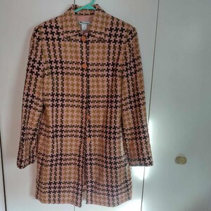 May include: A long, button-down coat with a houndstooth pattern in shades of pink, brown, and black. The coat is hanging on a green hanger against a white background. The coat has long sleeves and a collared neckline.