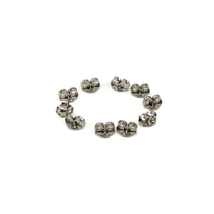 May include: A selection of silver-coloured earring backs, arranged in a circle against a white backdrop. The earring backs are butterfly-shaped, designed to secure earrings. The image is well-lit, showing the details of the jewellery findings.