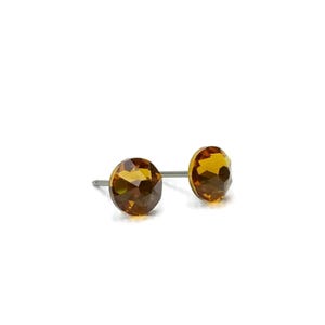 May include: A pair of stud earrings with faceted, amber-coloured gemstones. The earrings have a simple design with a post backing. The gemstones are round and have a sparkling appearance, set against a white background.