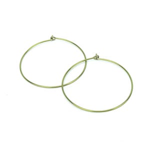 May include: Two gold-colored hoop earrings on a white background. The earrings are circular, with a simple, minimalist design. The hoops are thin and appear to be made of metal. The earrings are displayed close together, suggesting they are a pair.