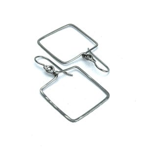 Peut inclure: Une paire de boucles d'oreilles carrées argentées. Les boucles d'oreilles présentent un design géométrique simple avec une forme carrée et une fermeture à crochet. Le métal a une texture légèrement martelée, ajoutant un intérêt visuel au style minimaliste.