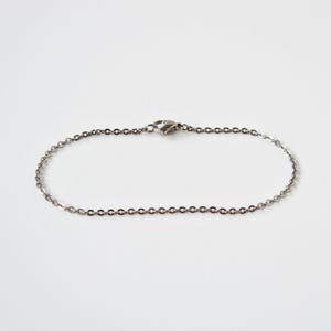 May include: A silver chain bracelet with a lobster clasp. The bracelet is composed of small, oval links. The jewellery is displayed on a white surface.