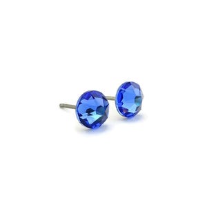 Può includere: Un paio di orecchini a lobo con gemme blu. Ogni orecchino presenta una gemma sfaccettata, rotonda, color zaffiro. Gli orecchini sono montati su perni color argento e sono esposti su sfondo bianco.