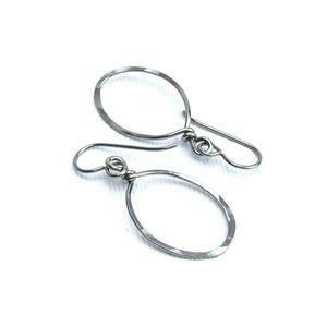 May include: A pair of silver-toned oval hoop earrings with hammered texture. The earrings have a simple, minimalist design with a hook closure. The jewelry is displayed on a white background.