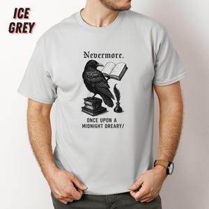 May include: Ice grey t-shirt featuring a black raven illustration with the text "Nevermore" and "Once Upon a Midnight Dreary/". The raven is perched on books, holding a book and quill.