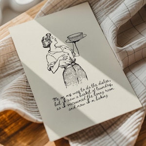 May include: A cream-colored greeting card with a black and white illustration of a woman holding a pie. The card has handwritten text that reads, "Me on my way to do the dishes, but I saw a basket of laundry, so I vacuumed the living room and now I'm baking."