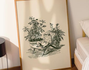Może przedstawiać: Oprawiony czarno-biały wydruk przedstawiający żabę wylegiwującą się na krześle pośród roślin doniczkowych. Nadruk ma jasnobrązową ramę. Na zdjęciu widoczna jest również czarna lampa, filiżanka kawy i łóżko.