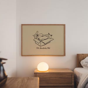 Minimal black line drawing of a cat lounging in a box, styled as a funny cat poster with homebody decor charm for a cozy book nook poster space, text reads “The Homebody Club”.