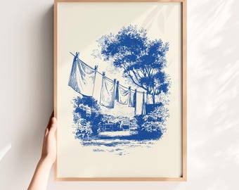 May include: Blue and white framed print depicting laundry hanging on a clothesline in a garden setting. The artwork features a detailed illustration of trees, bushes, and a pathway, creating a serene, vintage aesthetic.