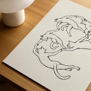 Physical matte paper art print featuring five hand drawn minimalist line art cats dancing in a circle, a funny modern cat poster parody inspired by Matisse. Black and white unframed sketchy pet print for girl apartment decor, scandi style wall art, and cozy bedroom layouts.