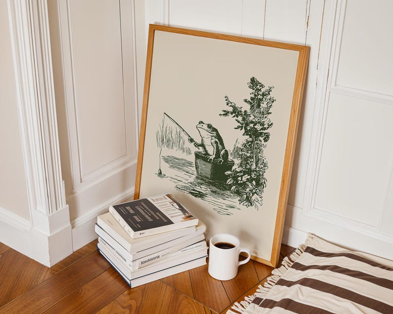 Hand drawn poster of a fishing frog sitting in a bucket by the water, ink drawing with vintage line art style, frog wall art for lake house decor, cabin decor, and fishing wall art.