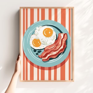 May include: A framed print featuring a breakfast scene. Two sunny-side-up eggs with bright yellow yolks and crispy bacon are on a light blue plate. The background has a red and white striped pattern.
