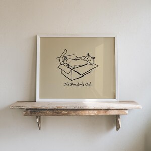 Minimal black line drawing of a cat lounging in a box, styled as a funny cat poster with homebody decor charm for a cozy book nook poster space, text reads “The Homebody Club”.