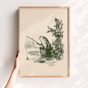 Hand drawn poster of a fishing frog sitting in a bucket by the water, ink drawing with vintage line art style, frog wall art for lake house decor, cabin decor, and fishing wall art.