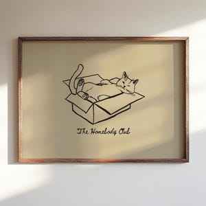 Minimal black line drawing of a cat lounging in a box, styled as a funny cat poster with homebody decor charm for a cozy book nook poster space, text reads “The Homebody Club”.