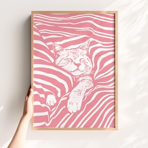Puede incluir: Impresión enmarcada con una ilustración de un gato durmiendo. El gato está representado en blanco sobre un fondo a rayas rosas y blancas. La obra de arte está en un marco de madera.