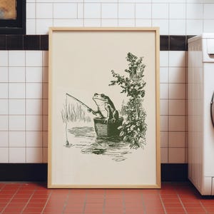 Hand drawn poster of a fishing frog sitting in a bucket by the water, ink drawing with vintage line art style, frog wall art for lake house decor, cabin decor, and fishing wall art.