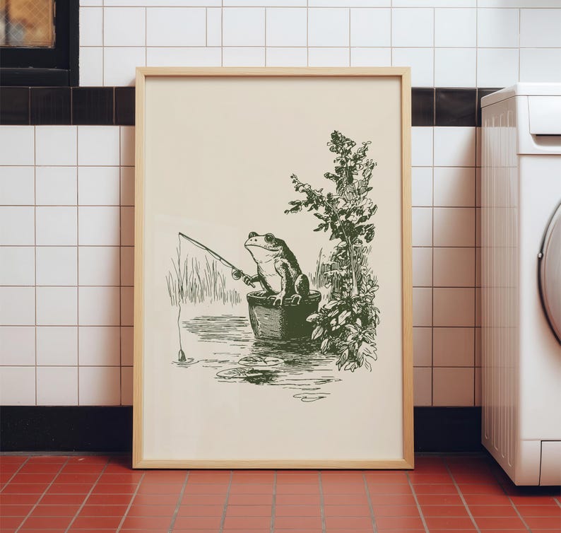 Hand drawn poster of a fishing frog sitting in a bucket by the water, ink drawing with vintage line art style, frog wall art for lake house decor, cabin decor, and fishing wall art.